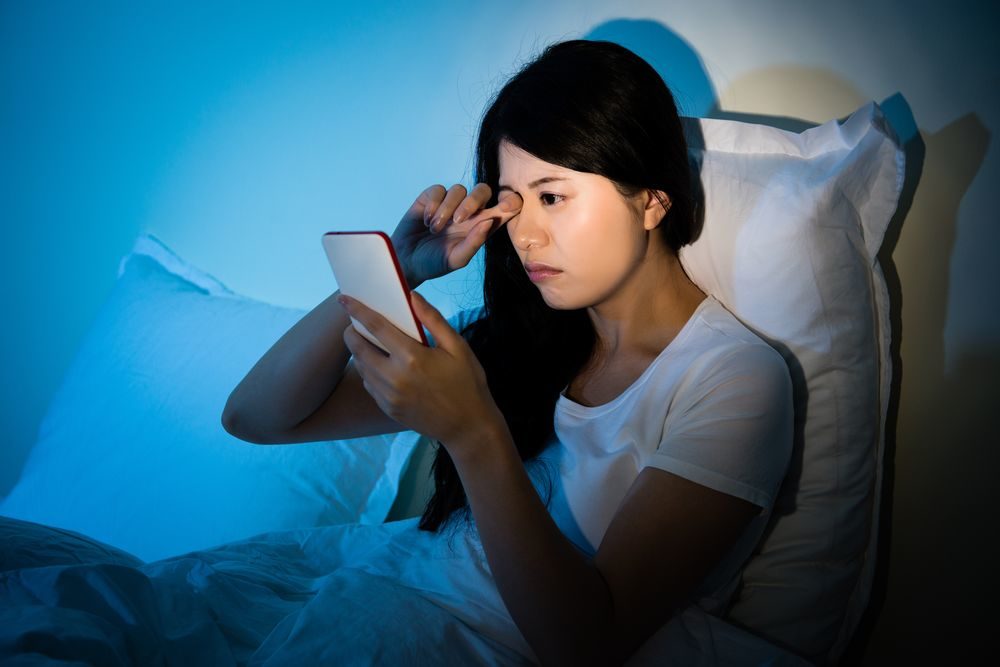 夜ベッドでスマホを見る女性の写真