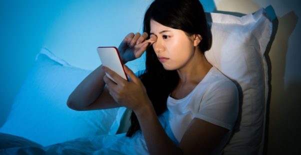 夜ベッドでスマホを見る女性の写真
