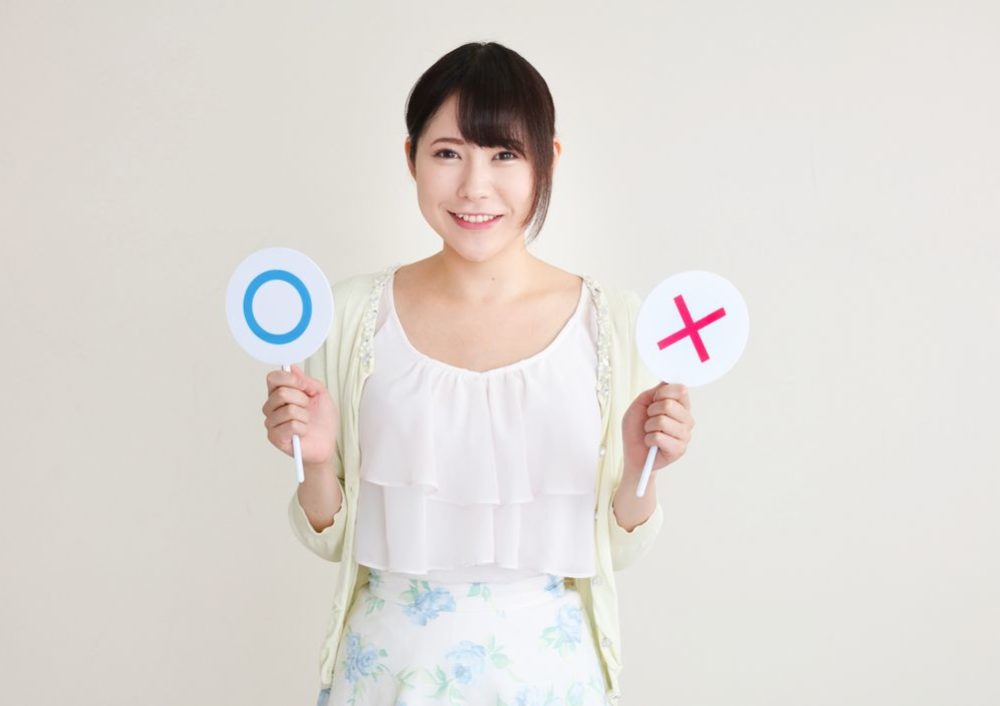 マルとバツの札を持つ女性の写真