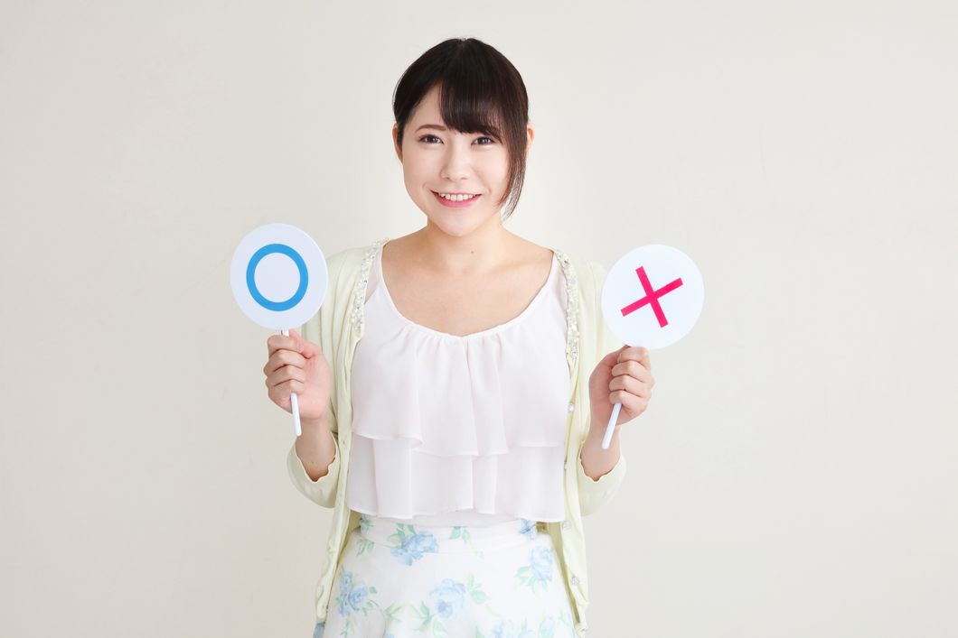 マルとバツの札を持つ女性の写真