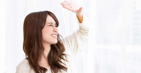 窓辺でまぶしそうにしている女性の写真