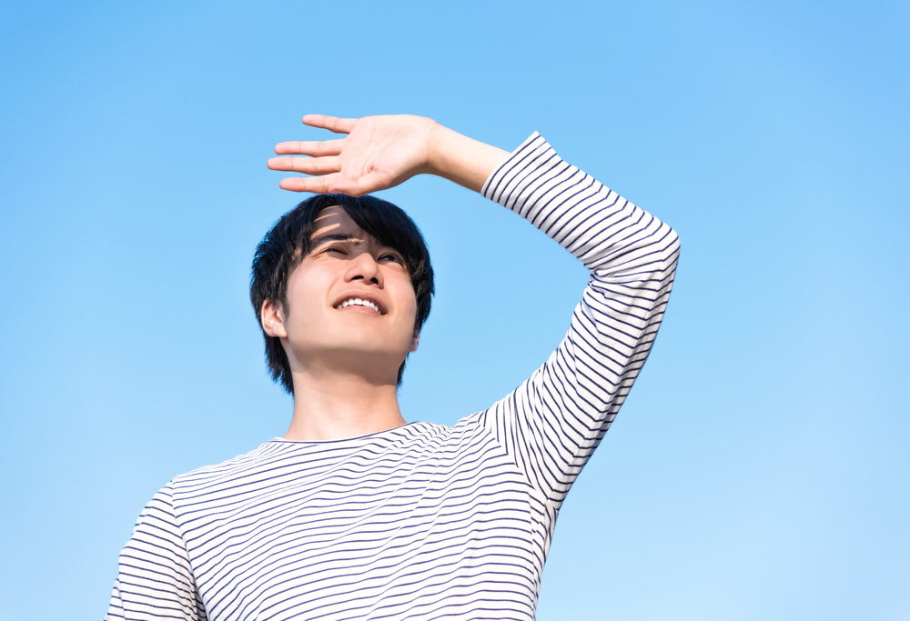 まぶしそうに空を見上げる男性の写真