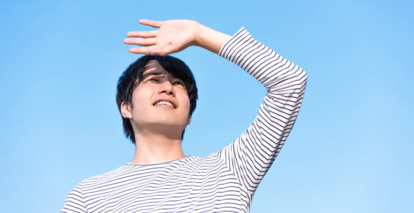まぶしそうに空を見上げる男性の写真