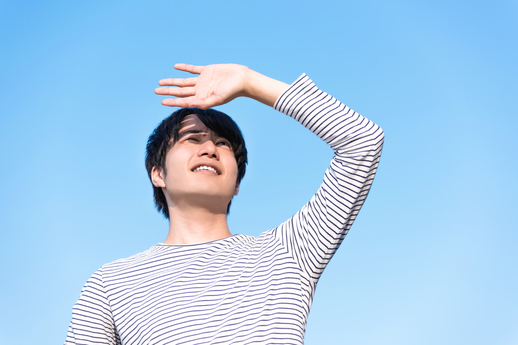 まぶしそうに空を見上げる男性の写真