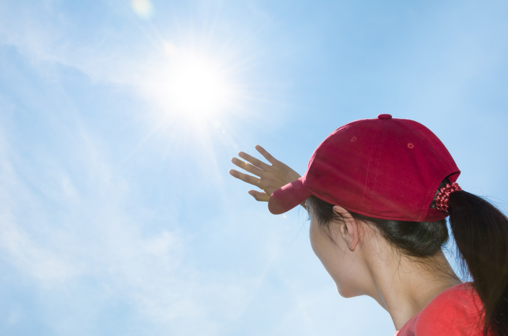 紫外線を浴び、帽子を被って手でまぶしさを防いでいる女性